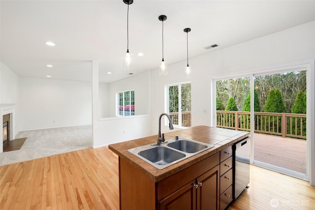 kitchen with visible vents, a fireplace with flush hearth, a sink, stainless steel dishwasher, and tile countertops