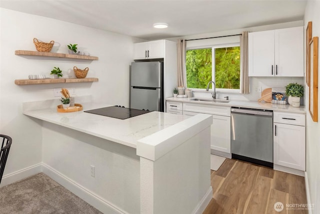 kitchen featuring light wood-style flooring, a sink, light stone counters, appliances with stainless steel finishes, and white cabinets