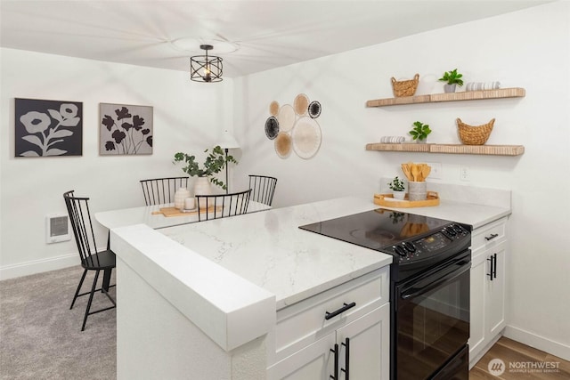 kitchen with light stone counters, black electric range oven, white cabinetry, and a peninsula