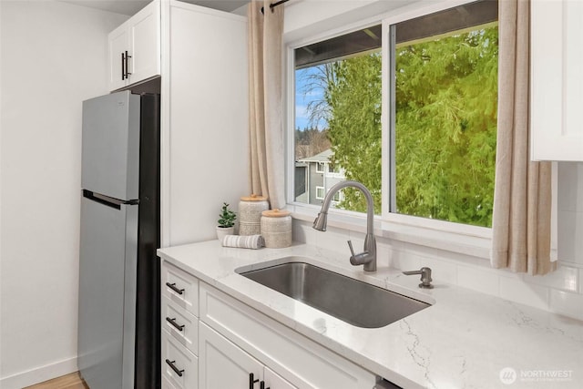 kitchen with plenty of natural light, light stone countertops, freestanding refrigerator, and a sink