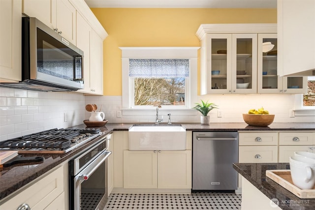 kitchen with appliances with stainless steel finishes, dark stone counters, glass insert cabinets, and a sink