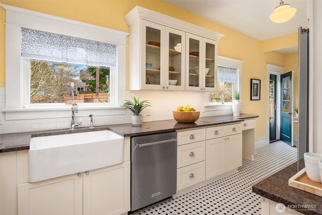 kitchen featuring dark stone countertops, a sink, decorative backsplash, glass insert cabinets, and stainless steel dishwasher