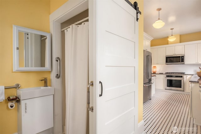 interior space with backsplash, pendant lighting, a barn door, white cabinets, and stainless steel appliances