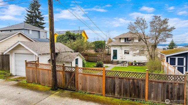 exterior space with a shingled roof, entry steps, fence private yard, a garage, and an outbuilding