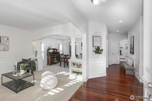 corridor featuring a decorative wall, wood finished floors, a wainscoted wall, and arched walkways