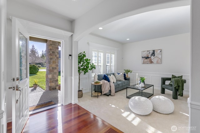 living room with wood finished floors, recessed lighting, arched walkways, wainscoting, and a decorative wall