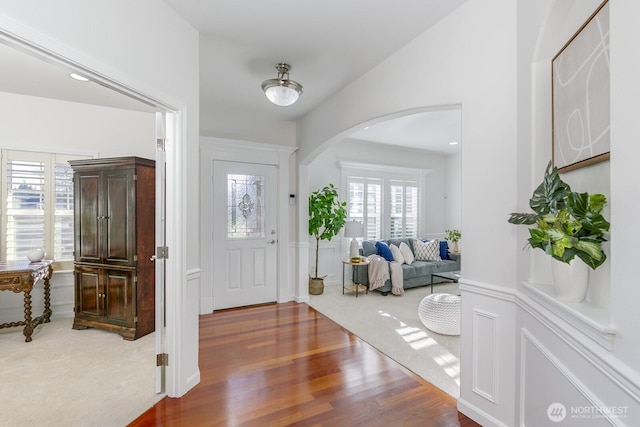 foyer entrance featuring arched walkways, a decorative wall, and wood finished floors