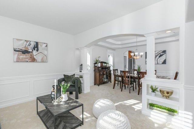 living room featuring arched walkways, wainscoting, a decorative wall, a raised ceiling, and a chandelier