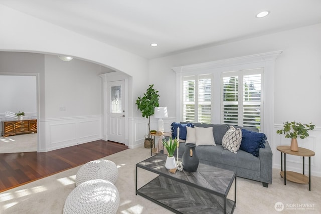 living area with a wainscoted wall, wood finished floors, recessed lighting, arched walkways, and a decorative wall