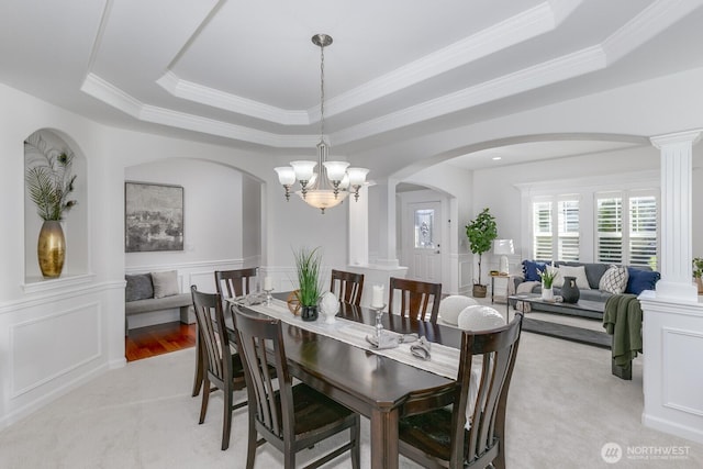 dining room featuring a raised ceiling, a decorative wall, and decorative columns