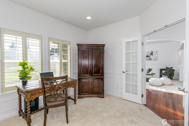 office area featuring a wainscoted wall, light carpet, french doors, arched walkways, and a decorative wall