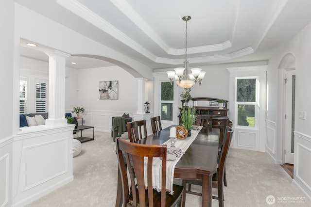 carpeted dining space featuring a wealth of natural light, a raised ceiling, a decorative wall, and ornate columns