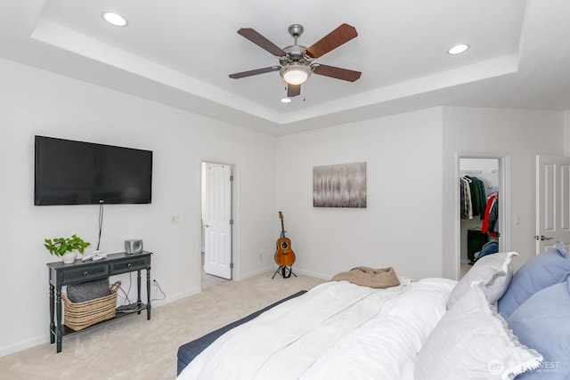 carpeted bedroom with recessed lighting, a tray ceiling, baseboards, and a walk in closet