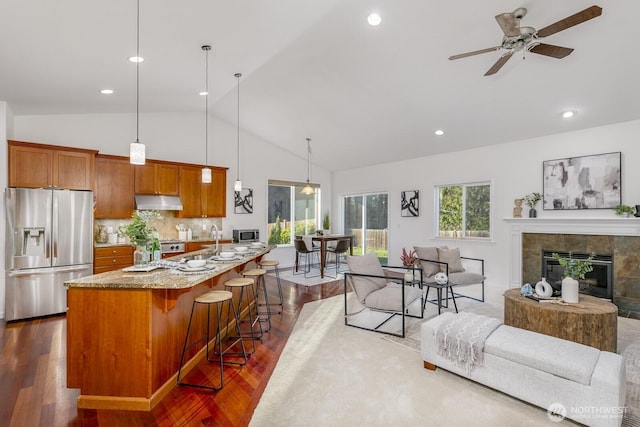 kitchen with under cabinet range hood, a breakfast bar, light stone counters, brown cabinetry, and stainless steel appliances