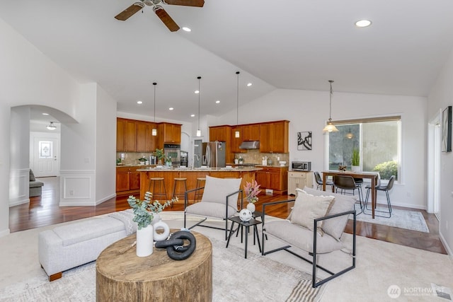 living area with lofted ceiling, recessed lighting, light wood-style floors, arched walkways, and a ceiling fan