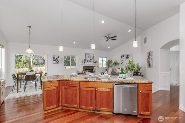 kitchen with open floor plan, stainless steel dishwasher, arched walkways, a glass covered fireplace, and a sink