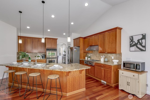 kitchen with a breakfast bar, under cabinet range hood, a sink, appliances with stainless steel finishes, and brown cabinetry