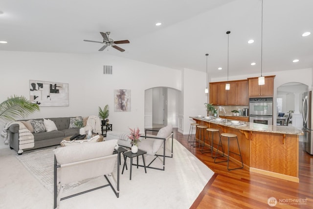 living area featuring recessed lighting, visible vents, arched walkways, and light wood-style floors