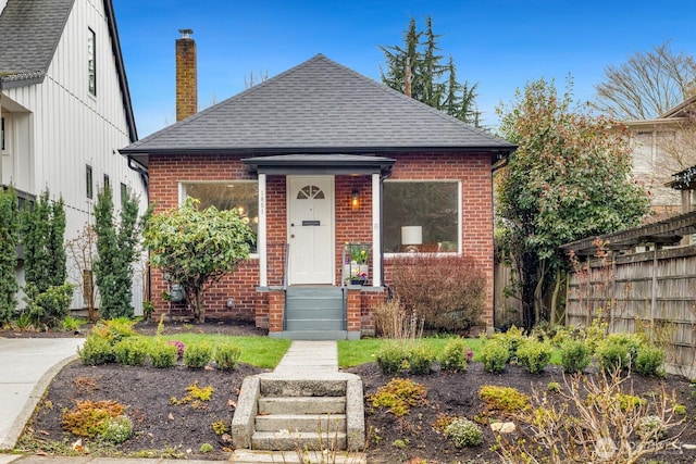 view of front of property with a chimney, fence, brick siding, and a shingled roof