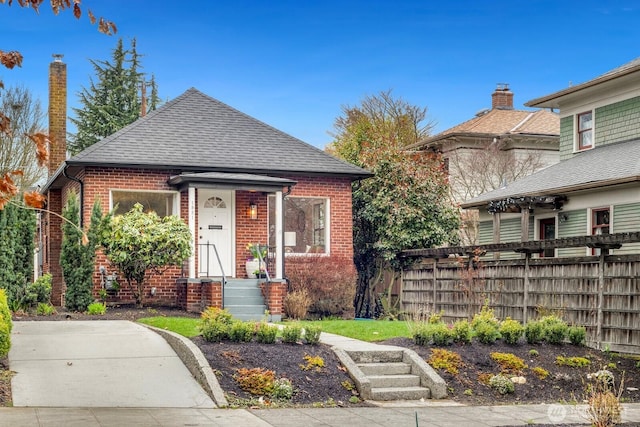 view of front of home featuring brick siding, roof with shingles, and fence