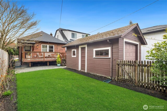 rear view of house featuring a yard, a deck, a garage, an outdoor structure, and a fenced backyard