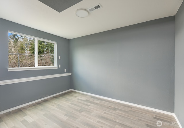 empty room with wood finished floors, visible vents, and baseboards