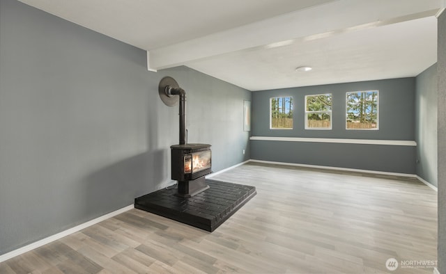 living area with beam ceiling, a wood stove, wood finished floors, and baseboards