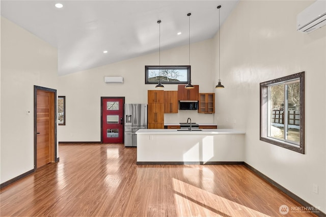 kitchen with brown cabinetry, a peninsula, a sink, an AC wall unit, and appliances with stainless steel finishes