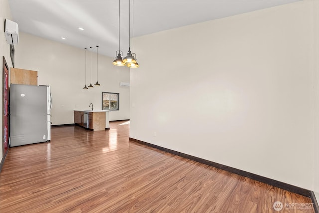 interior space featuring a sink, a wall unit AC, light wood-style floors, a high ceiling, and baseboards