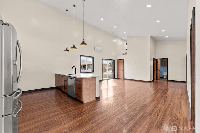 kitchen featuring dark wood finished floors, open floor plan, a peninsula, stainless steel appliances, and a sink