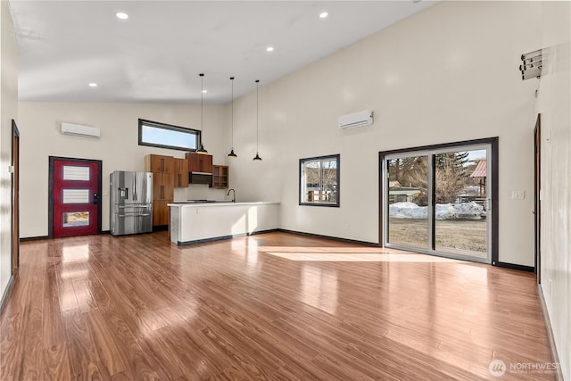 unfurnished living room with a healthy amount of sunlight, high vaulted ceiling, a wall mounted AC, and wood finished floors