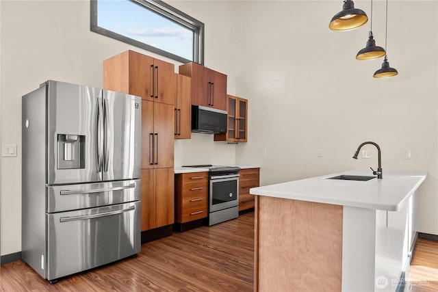 kitchen featuring brown cabinets, a sink, appliances with stainless steel finishes, a peninsula, and dark wood-style flooring