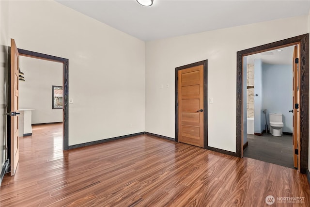 unfurnished bedroom with baseboards, wood finished floors, and ensuite bathroom