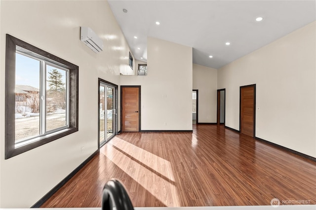 empty room featuring baseboards, a high ceiling, wood finished floors, and a wall unit AC