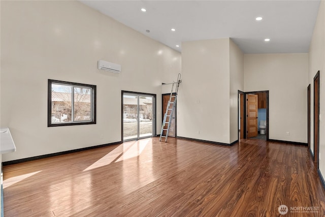 spare room featuring recessed lighting, an AC wall unit, baseboards, and wood finished floors