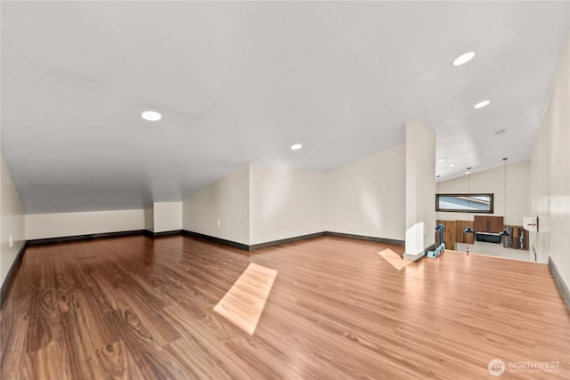 unfurnished living room with vaulted ceiling, recessed lighting, wood finished floors, and baseboards