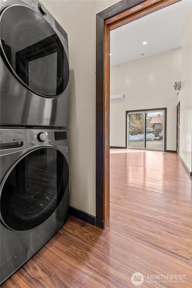 laundry room featuring stacked washer and clothes dryer, a wall mounted AC, wood finished floors, baseboards, and laundry area