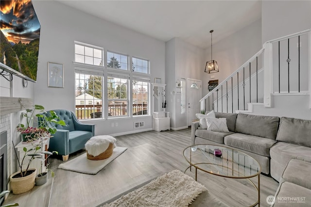 living room featuring wood finished floors, a glass covered fireplace, a high ceiling, baseboards, and stairs