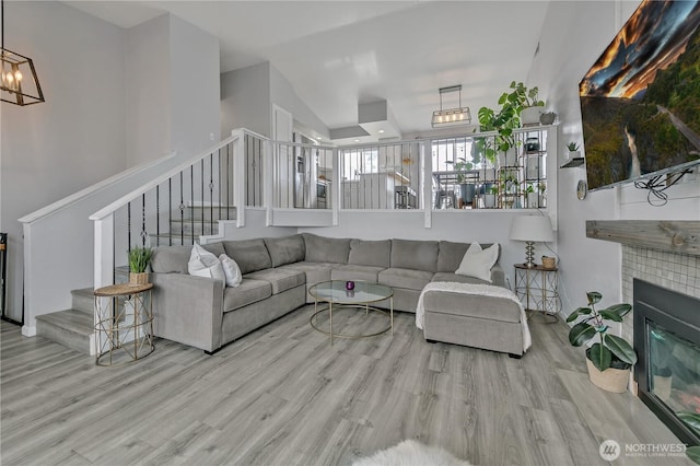 living room with stairs, a notable chandelier, wood finished floors, and a tile fireplace