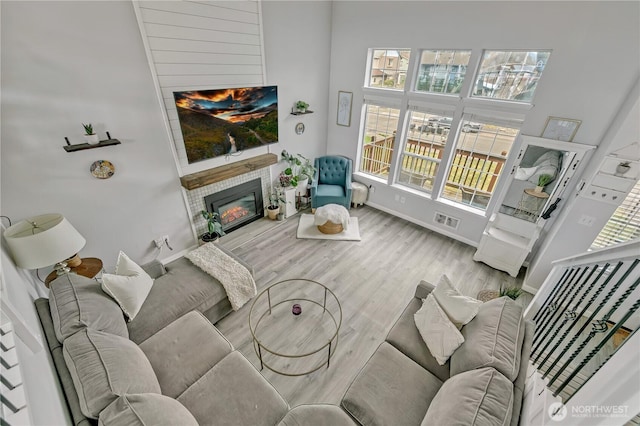 living room with a glass covered fireplace, baseboards, visible vents, and wood finished floors