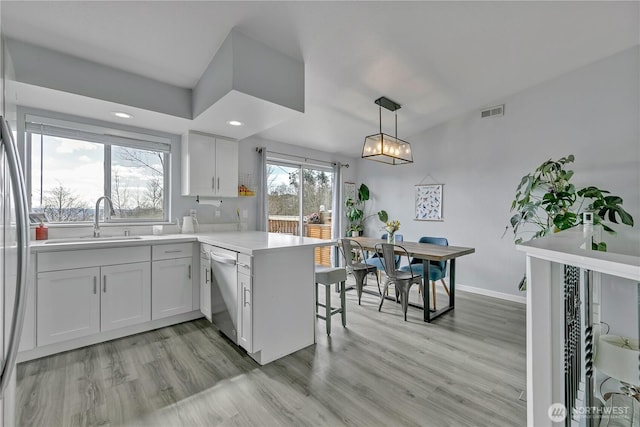 kitchen featuring a peninsula, a sink, light countertops, appliances with stainless steel finishes, and white cabinetry