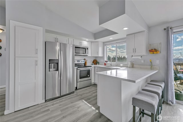 kitchen featuring a kitchen breakfast bar, appliances with stainless steel finishes, a peninsula, white cabinets, and a sink