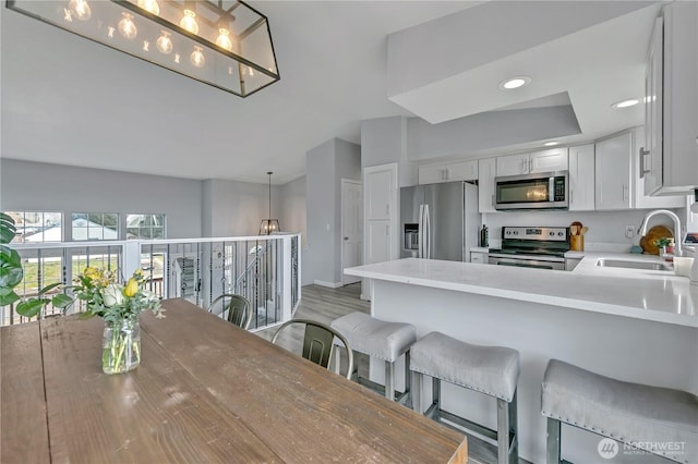 kitchen featuring a breakfast bar, light countertops, appliances with stainless steel finishes, white cabinets, and a sink