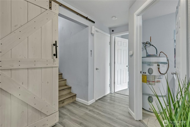 interior space featuring a barn door, wood finished floors, water heater, and baseboards