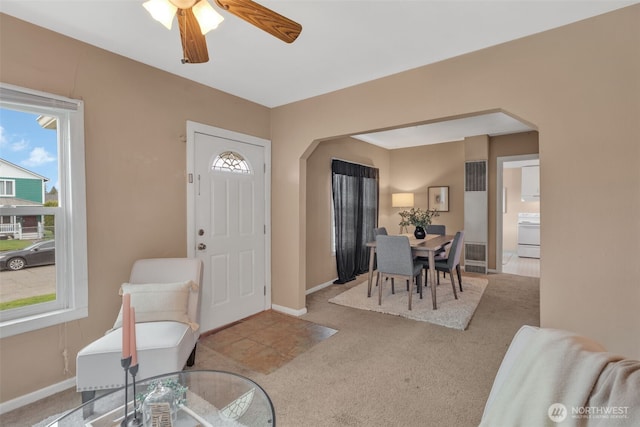 carpeted foyer entrance with arched walkways, a ceiling fan, and baseboards