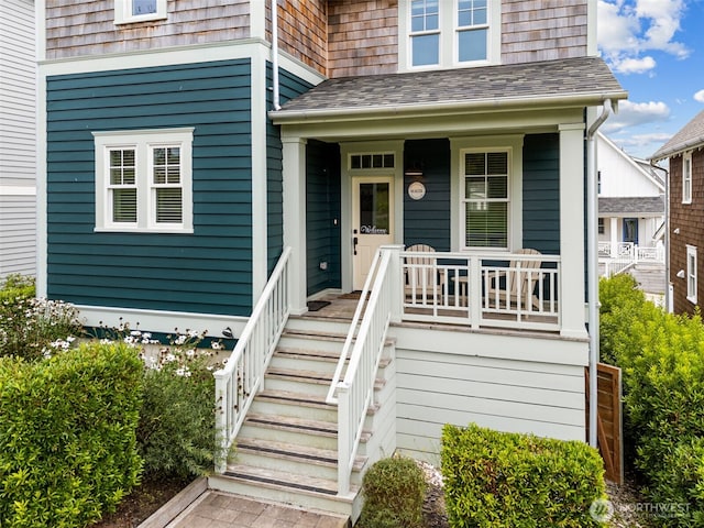 property entrance featuring covered porch and a shingled roof