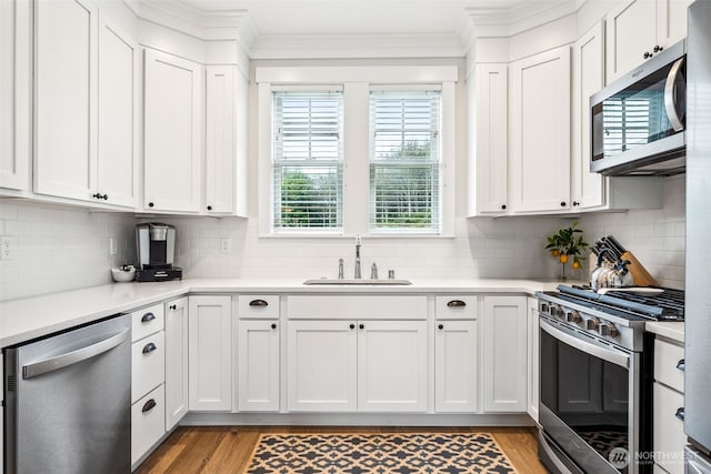 kitchen featuring crown molding, white cabinets, appliances with stainless steel finishes, and a sink