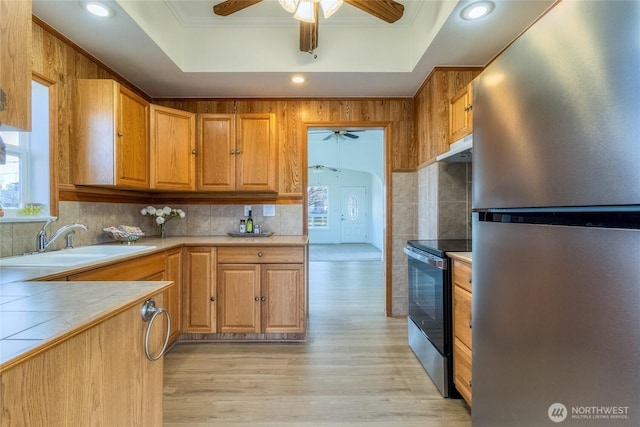 kitchen with ornamental molding, a sink, a tray ceiling, appliances with stainless steel finishes, and light wood finished floors