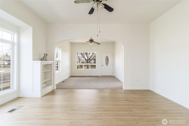 interior space featuring a wealth of natural light, visible vents, arched walkways, and light wood-style floors