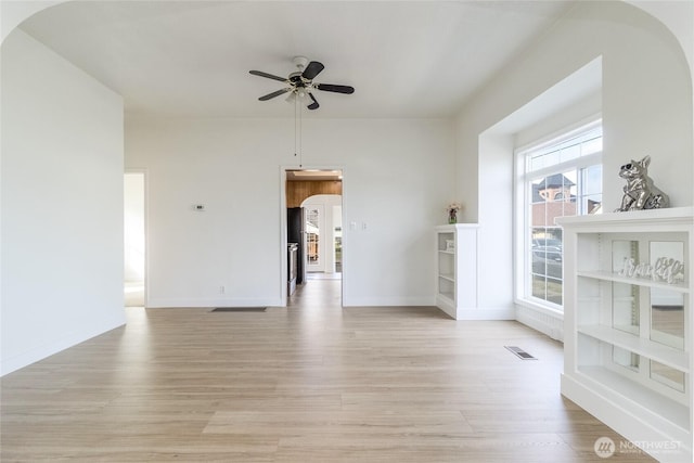 unfurnished room featuring a ceiling fan, light wood-style floors, visible vents, and arched walkways